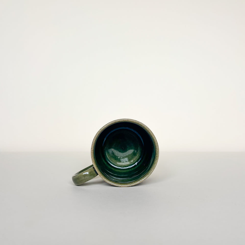 Green ceramic mug on a cream background. Pottery Mug  Handmade in Ireland. Wheel Thrown Pottery and Ceramic.