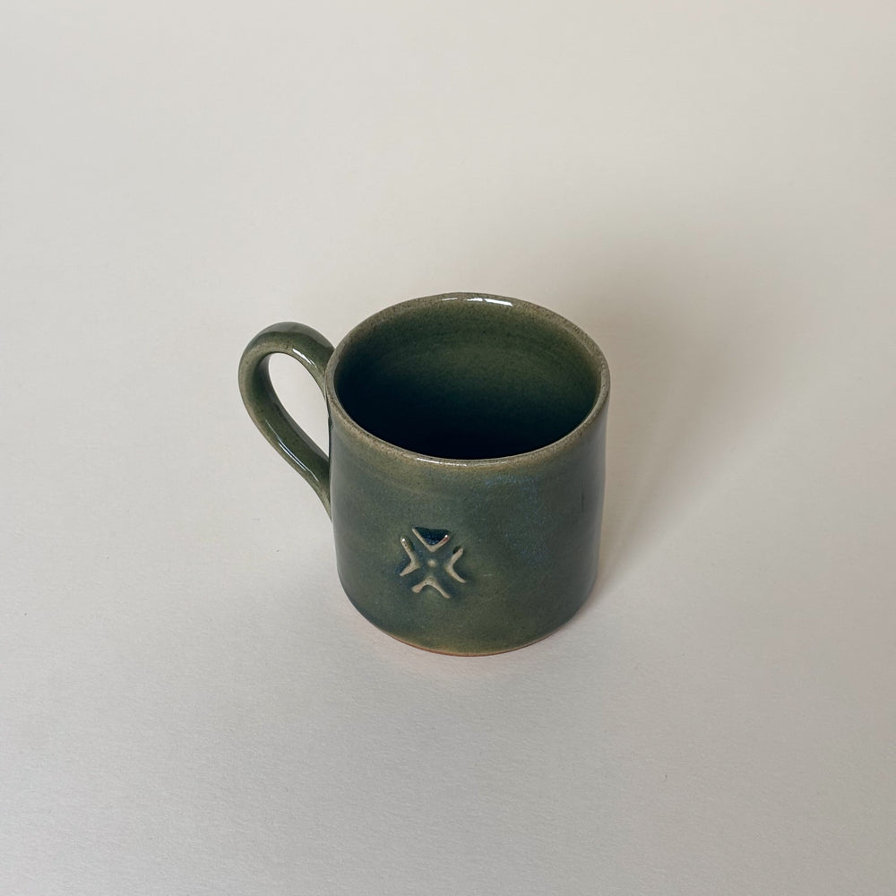 Green ceramic mug with an amazonian symbol design on a cream background. Pottery Mug  Handmade in Ireland. Wheel Thrown Pottery and Ceramic. 