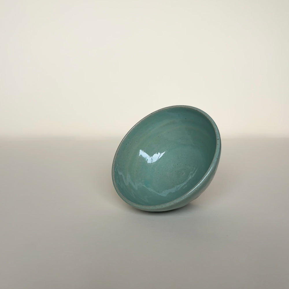 Green ceramic bowl on a cream beige background, showing smooth inner curve. Pottery bowl  Handmade in Ireland. Wheel Thrown Pottery and Ceramic.