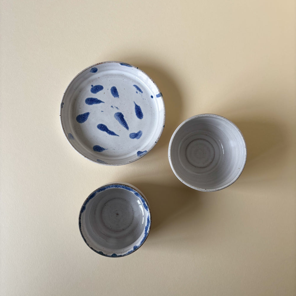 Two white ceramic bows and a white small plate  with blue patterns on a cream background. Pottery Handmade in Ireland. Wheel Thrown Pottery and Ceramic. 