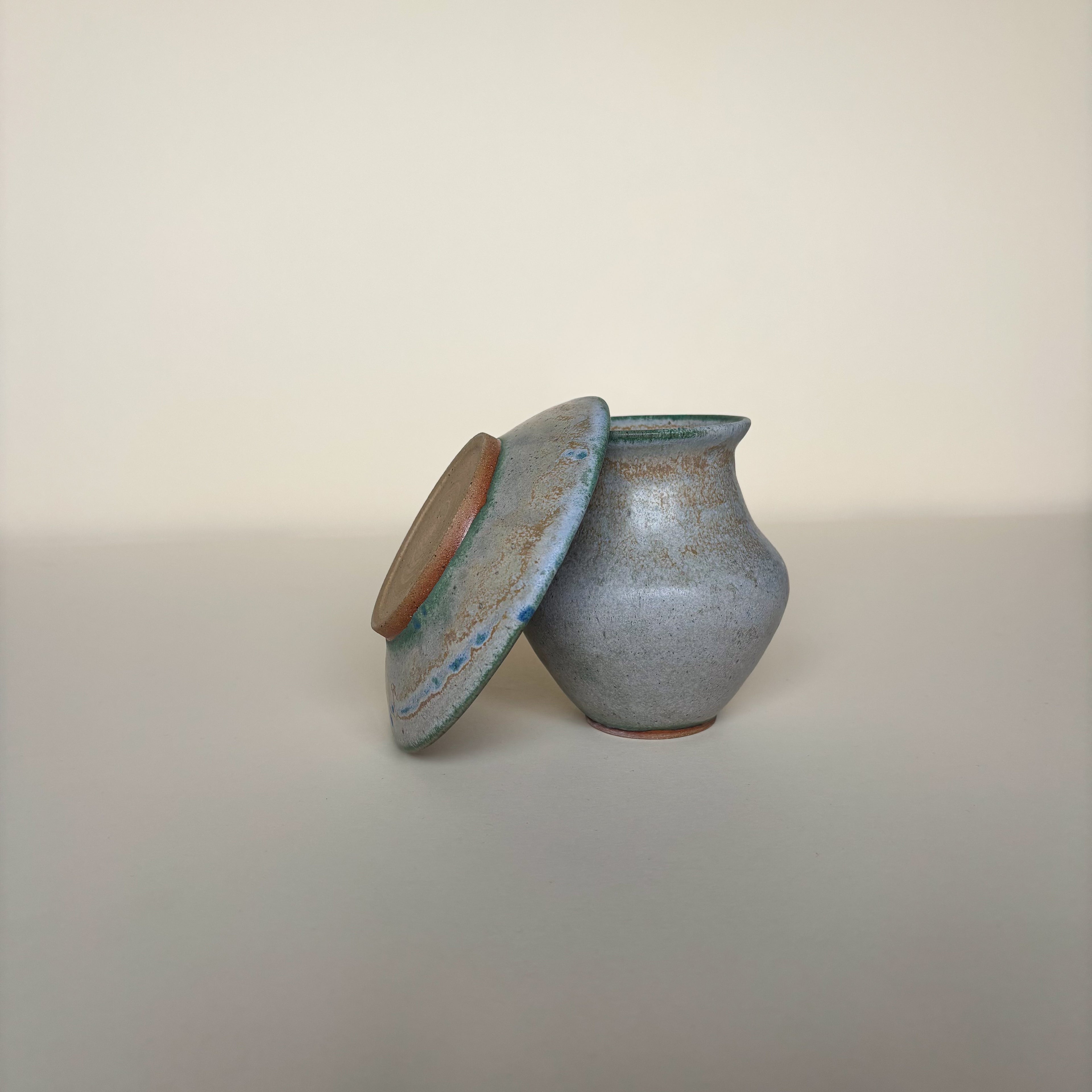 Handmade Wheel Thrown Small Gray Pottery Vase and Plate, with green, blue and yellow details and a matt to satin finish on a light cream background. 