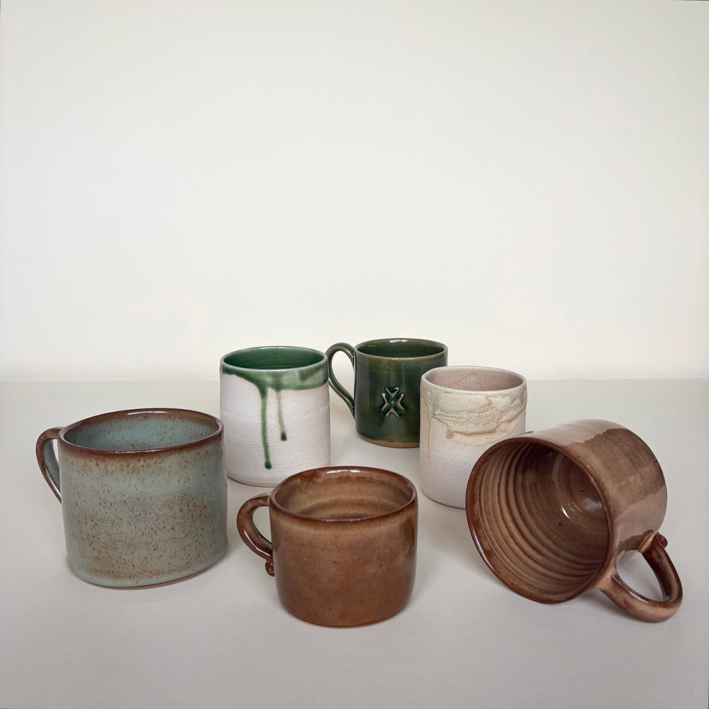 Set of six ceramic mugs and cups  in various colours on a cream background. Pottery Mugs and cups Handmade in Ireland. Wheel Thrown Pottery and Ceramic. 