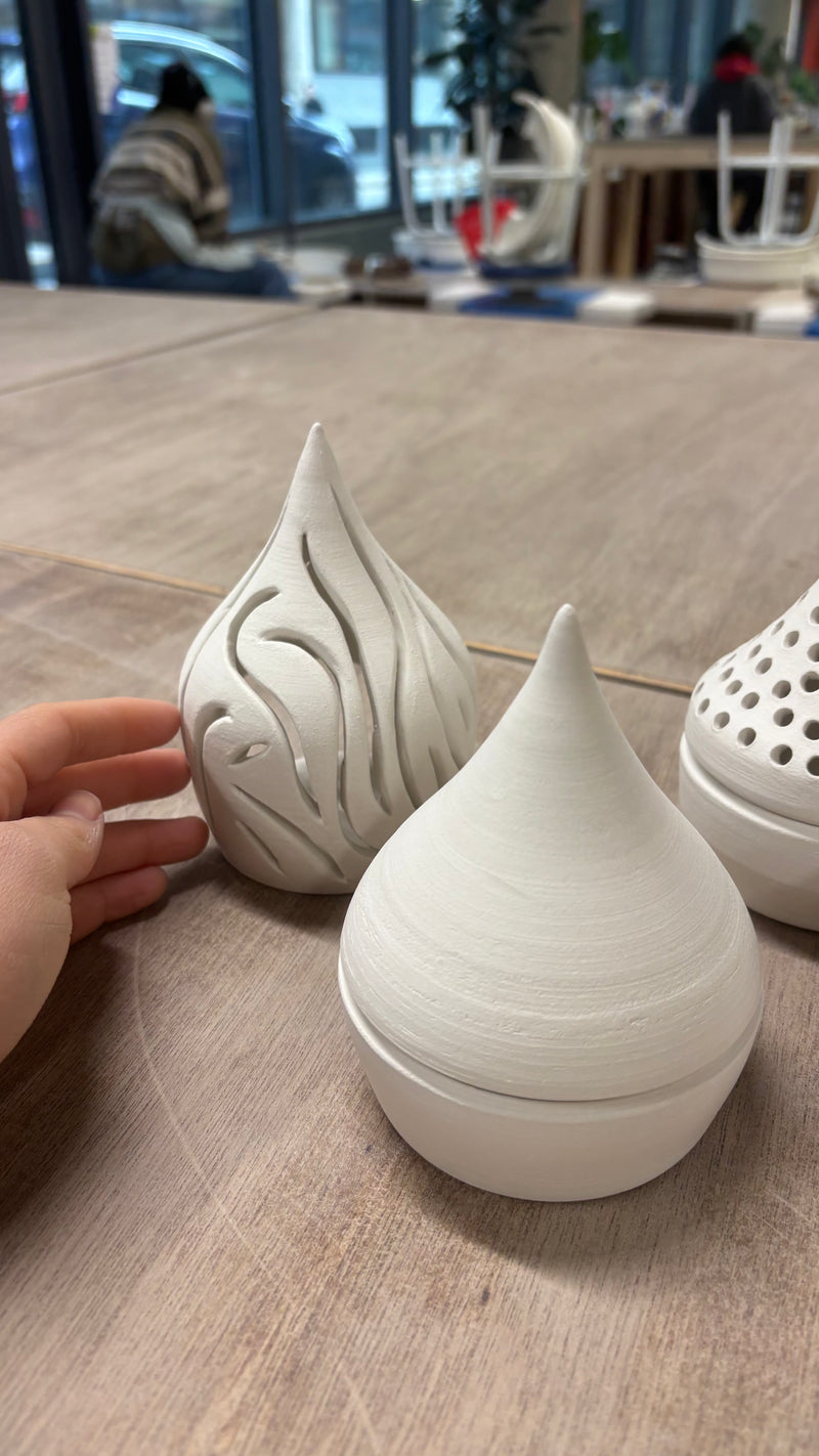 Three ceramic teardrop-shaped vases on a wooden surface with a blurred indoor background.