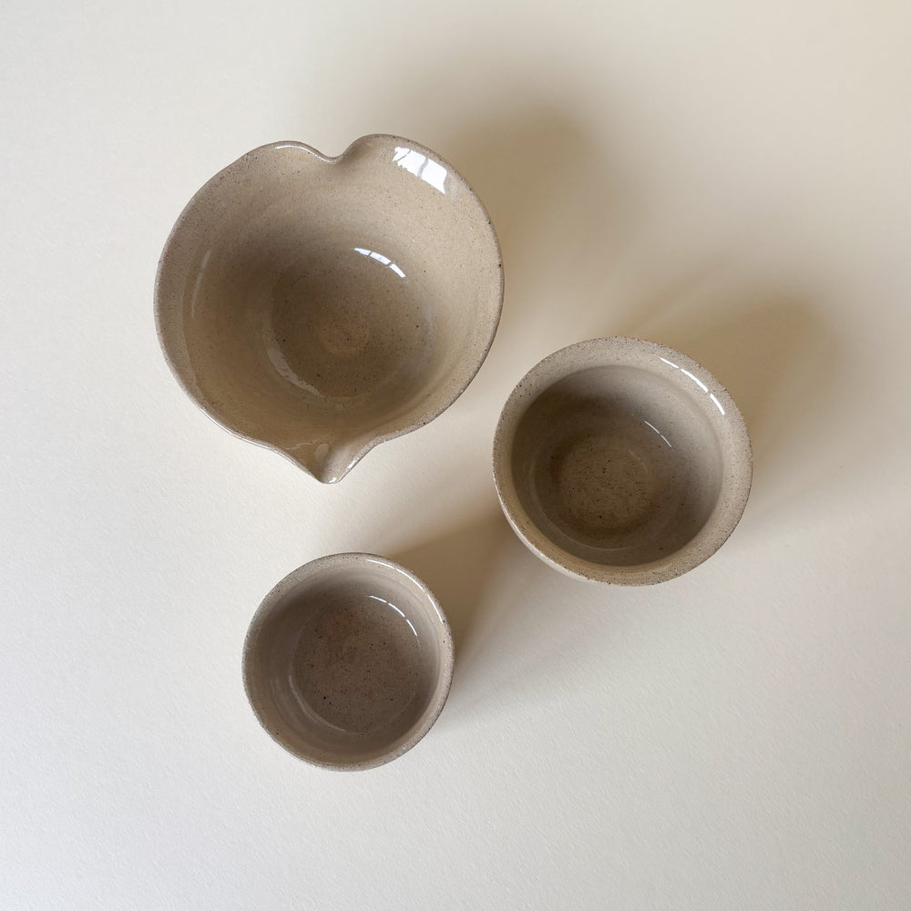 Three ceramic bowls of different sizes on a light cream background. Handmade Ceramic Pots, Natural clay colour, shiny finish. On a light background. Pottery Handmade in Ireland. Wheel Thrown Pottery and Ceramic. Including a handmade matcha bowl with a spout. 