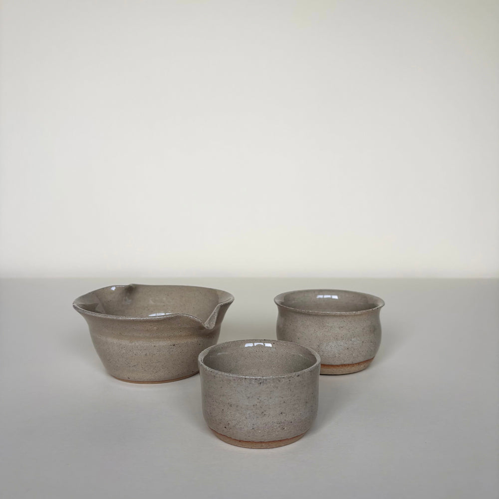 Three ceramic bowls of varying sizes on a light cream background front view. Handmade Ceramic Pots, Natural clay colour, shiny finish. On a light background. Pottery Handmade in Ireland. Wheel Thrown Pottery and Ceramic. Including a handmade matcha bowl with a spout. 
