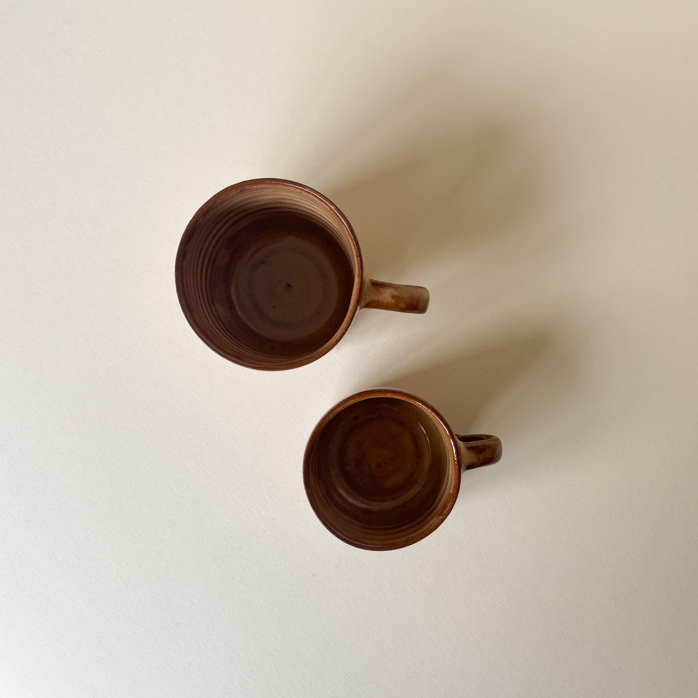 Two brown ceramic mugs on a light beige background. 