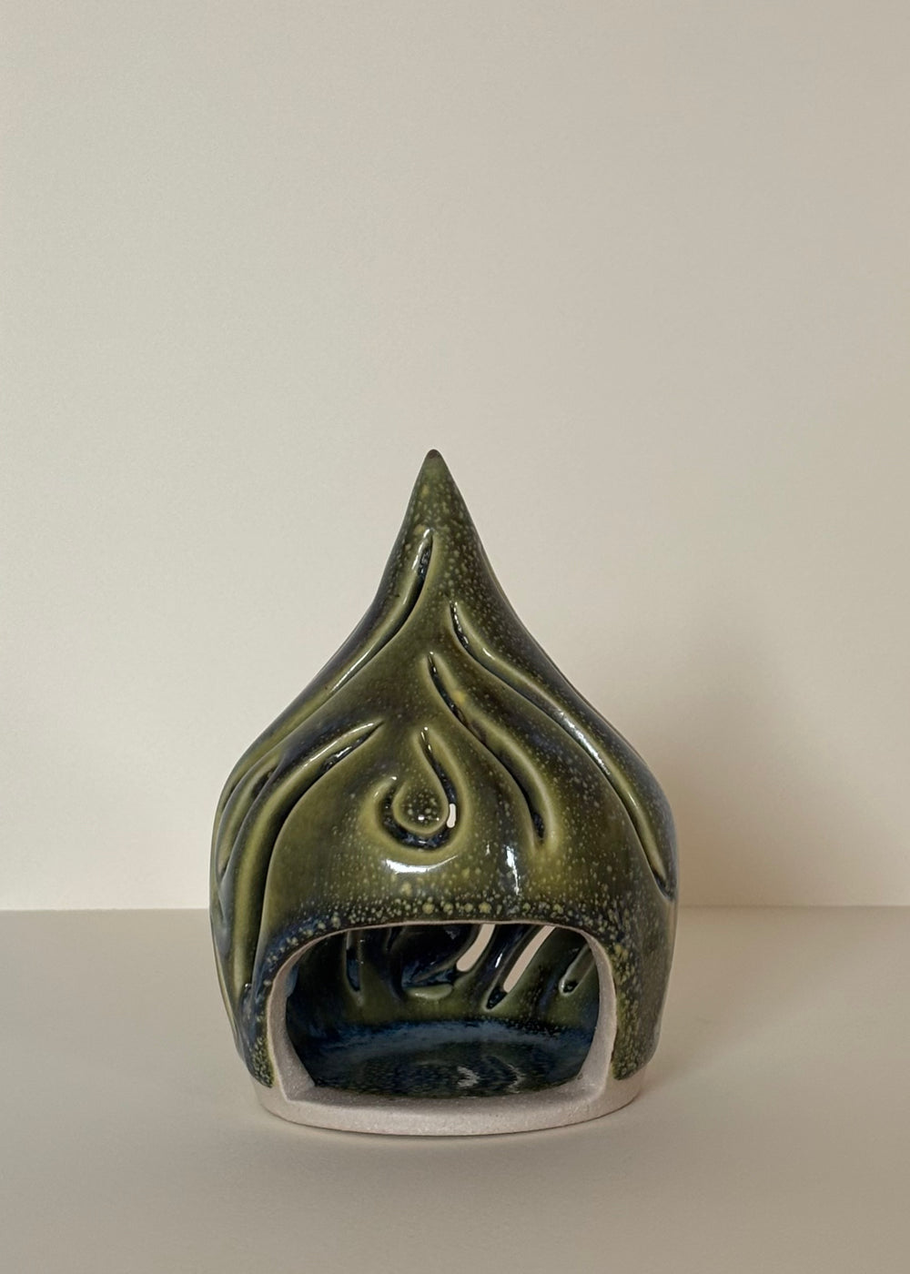 Green coloured ceramic tea light candle holder with a pointy design with carved wavy lines  on a light beige  background. Pottery  Handmade in Ireland. Wheel Thrown Pottery and Ceramic. 