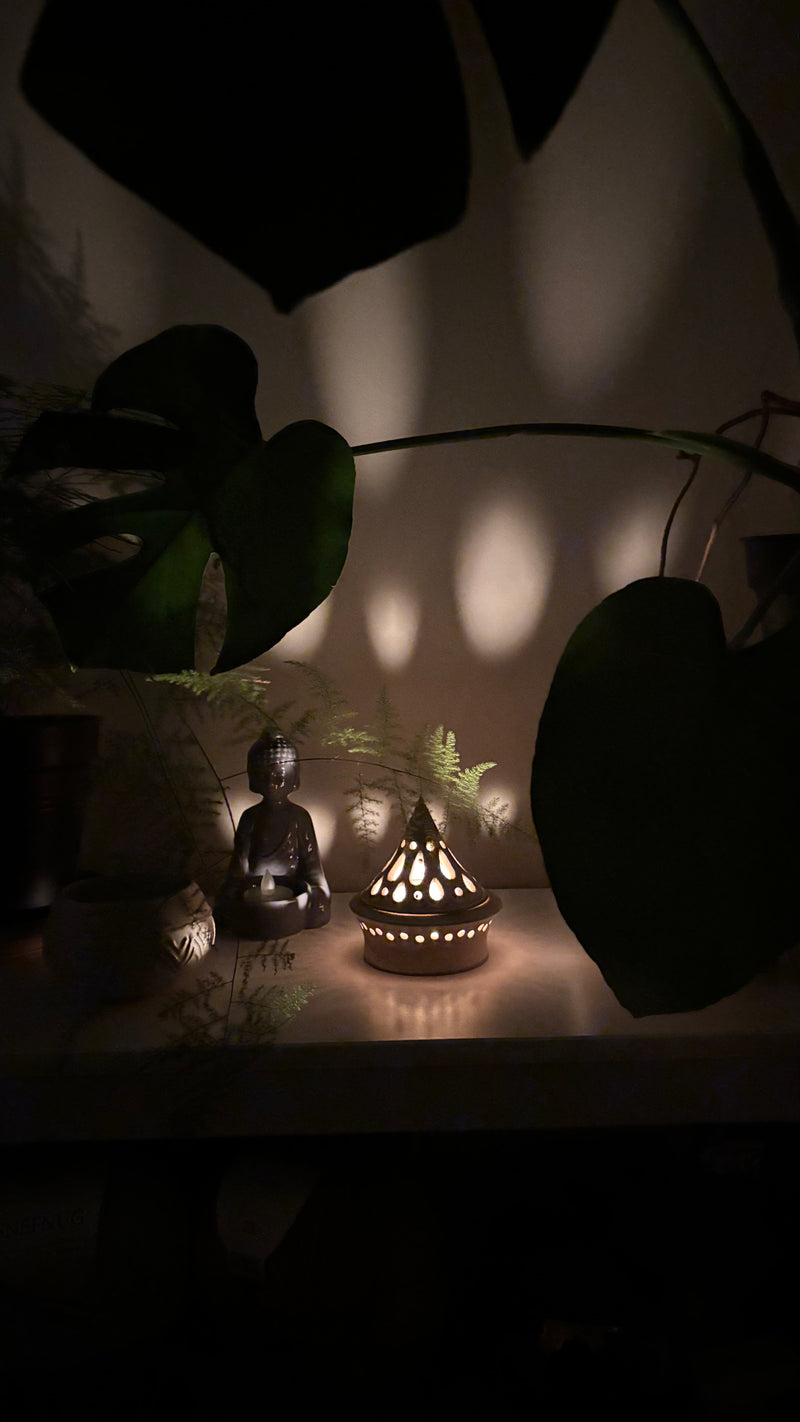 Decorative setup with a ceramic handmade tea light holder and lit candle, Buddha statue, and plants in a dimly lit room. Pottery  Handmade in Ireland. Wheel Thrown Pottery and Ceramic. 