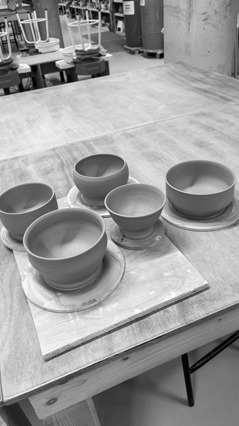 Set of ceramic bowls on a wooden table in a workshop setting. Handmade Wheel Throwing Pottery Bowls in Ireland.